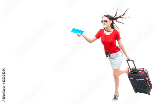 A young beautifull woman in sunglasses, a red blouse and a white skirt, with binoculars around her neck, holding a flight ticket and a small travel suitcase, on a white background, isolated.