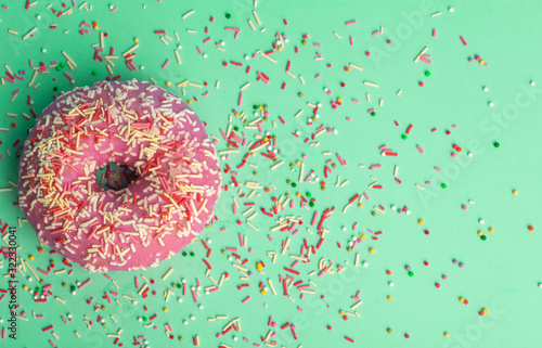 Donut (doughnut) of different colors on a green background with multi-colored festive sugar sprinkles. Holiday and sweets, baking for children, sugar concept