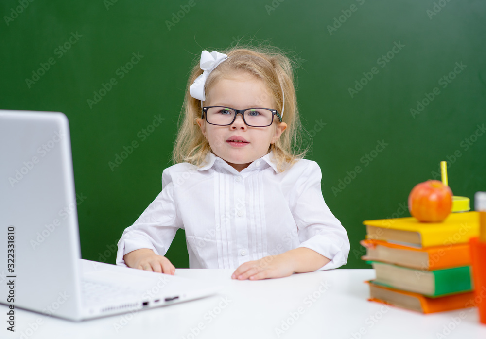Cute little girl in glasses is typing in concentration on a laptop in class at school, an apple lies with her Cute little girl in glasses is typing in concentration on a laptop in class at school, an apple lies with her