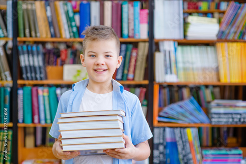 A cute boy in the library is standing with a stack of books in his hands. smiling looking in frame