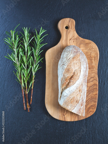 Artisan sourdough bread -  crusty baguette on the rustic slate and olive wood board, fresh herbs. Creative idea, copy space. photo