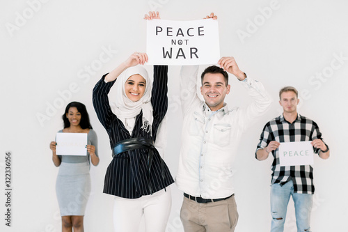 Young four people activists of different nationalities hold slogans for peace, no war and earth protection. Muslim girl and Caucasian man standing in front of friends and smiling. Isolated on white photo