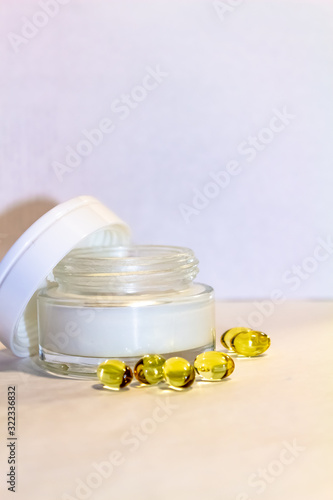 Face cream in a gold jar with gold capsules on a light background.