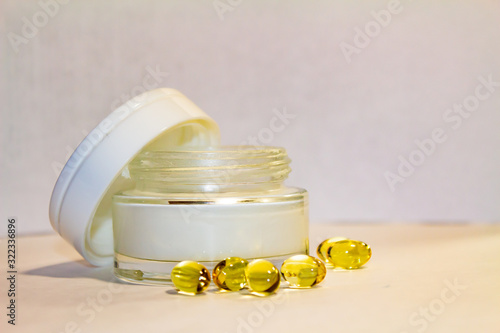 Face cream in a gold jar with gold capsules on a light background.