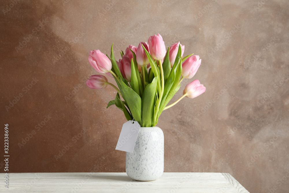 Vase with tulips on wooden table, space for text