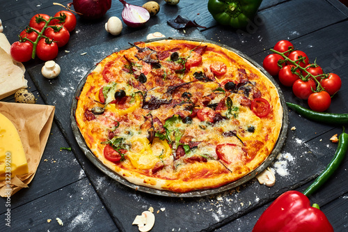 Pizza with mozzarella cheese, tomatoes, mushrooms, peppers, herbs on a dark wooden background.
