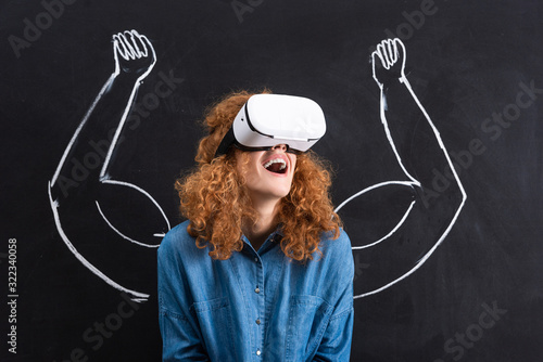 excited girl using virtual reality headset with strong arms drawing on blackboard