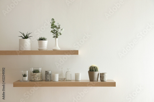 Wooden shelves with plants and decorative elements on light wall photo