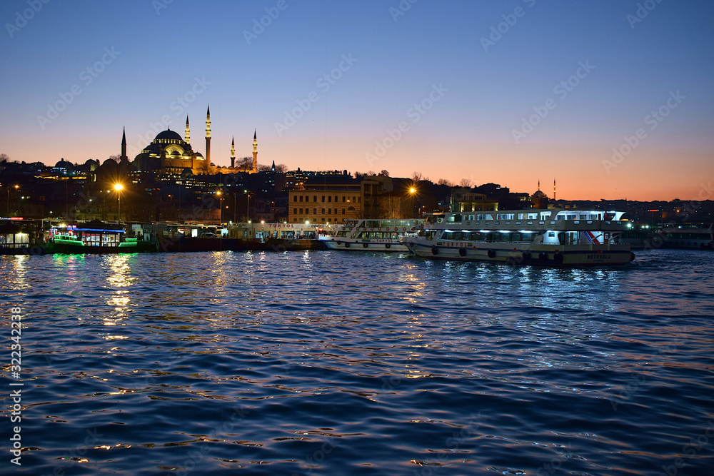 Suleymaniye Mosque in Istanbul after sunset. Istanbul lights reflected in the water. The ship sailing along the bay Golden Horn.
