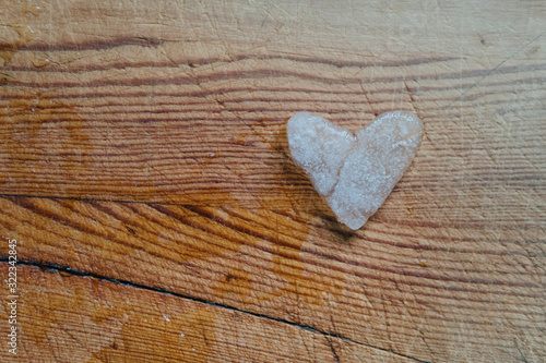 Snowy heart melts on a wooden table. Heart shaped snowball on a wooden kitchen cutting board. Ice in frosty weather. Melted water in the form of drops. Love on valentine s day concept