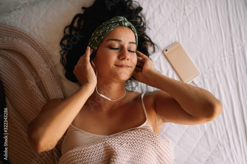 Beautiful woman lying on bed and listening music. 