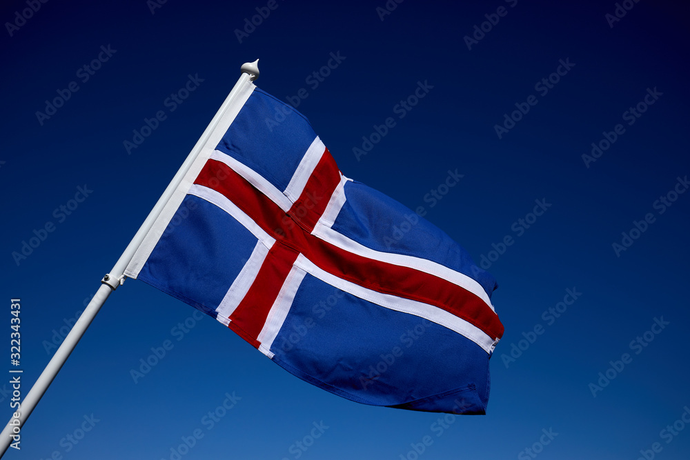 The flag of Iceland spreads in the wind on the clear blue sky background. Traveling concept background. Postcard