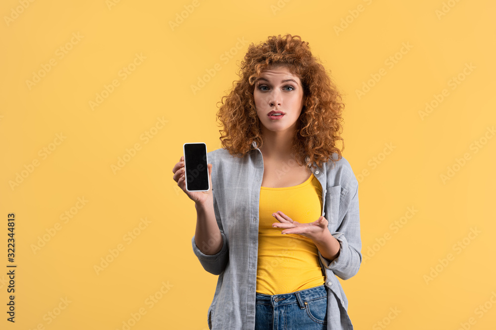 confused redhead woman showing smartphone with blank screen, isolated on yellow confused redhead woman showing smartphone with blank screen, isolated on yellow
