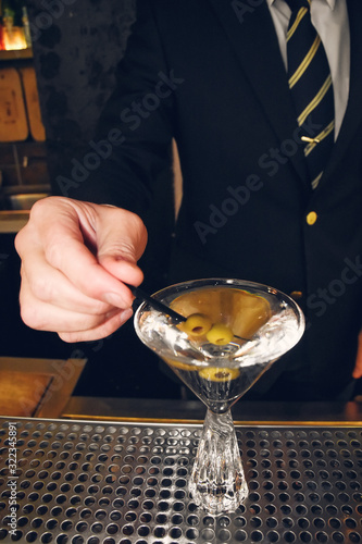 Male bartender or barman offering martini alcohol beverage, cocktail or drink with green olives in bar, nightclub, restaurant or pub