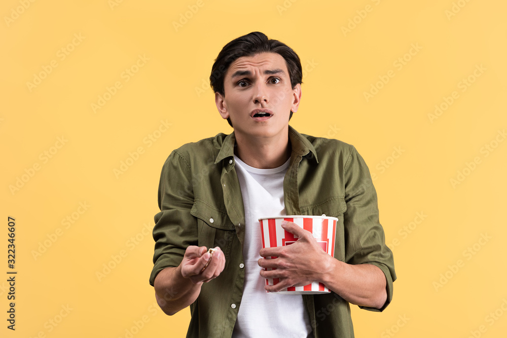 shocked young man watching movie with bucket of popcorn, isolated on yellow shocked young man watching movie with bucket of popcorn, isolated on yellow