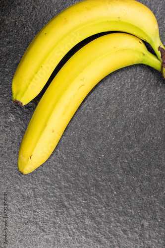 Two bananas joined together on a black plane. Exotic fruit, yellow bananas on a black stone surface. Bananas