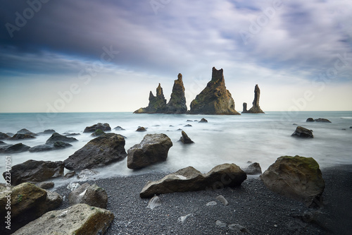 Famous tourist landscape with basalt rock formations Troll toes (Trolls fingers) on black beach. Ocean waves flow around stones. Reynisdrangar, Vik, Iceland, Atlantic Ocean, Europe. Travel postcard.