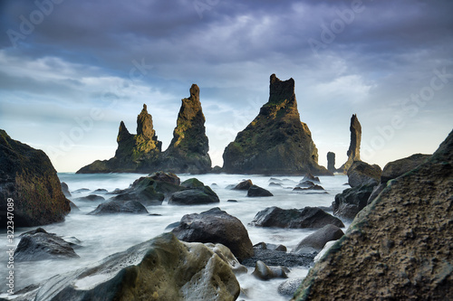 Famous tourist landscape with basalt rock formations Troll toes (Trolls fingers) on black beach. Ocean waves flow around stones. Reynisdrangar, Vik, Iceland, Atlantic Ocean, Europe. Travel postcard.