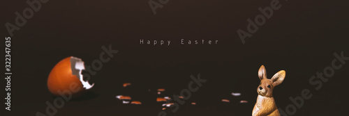 Easter egg, eggshell and bunny on dark background with copyspace and text. Banner of moody minimalistic decoration concept. Stock photo.