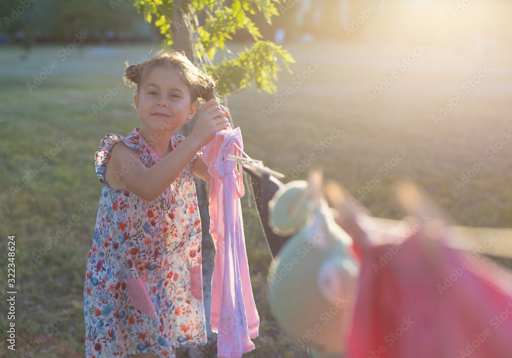 horizontal photo of a six-year-old pretty girl who hangs washed clothes ...