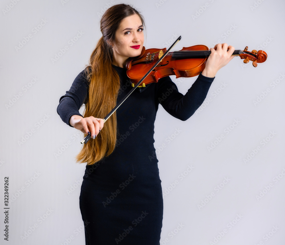 Portrait of a pretty brunette musician girl with a smile in a black dress on a white background holds a violin in her hands Portrait of a pretty brunette musician girl with a smile in a black dress on a white background holds a violin in her hands