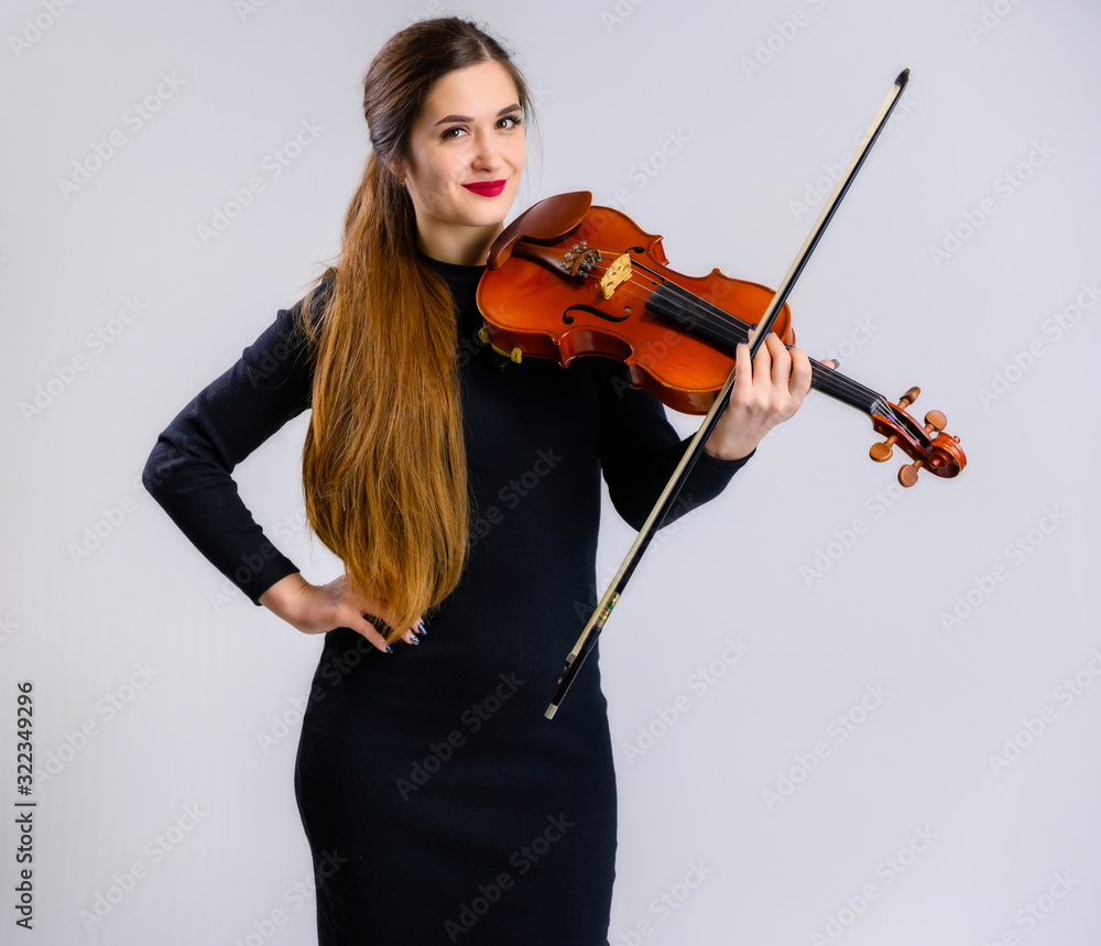 Portrait of a pretty brunette musician girl with a smile in a black dress on a white background holds a violin in her hands