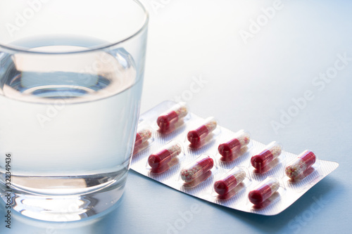 Capsules in blister with water in a clear glass cup on a grey surface. Medicine concept.