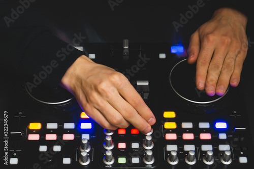 DJ plays music. sound mixer controller with knobs and sliders. hands on the mixing deck with turntables at dark with illuminated controls