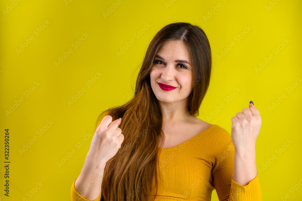nice brunette girl with long hair with a smile in a yellow jacket rejoices on a yellow background, smiles and shows positive emotions nice brunette girl with long hair with a smile in a yellow jacket rejoices on a yellow background, smiles and shows positive emotions