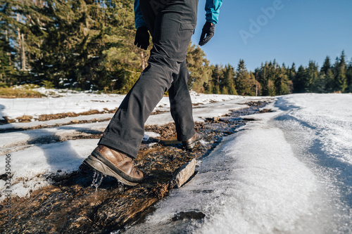 Trekking or hiking on a wet trail. Close up shot of hiking boots or shoes. Outdoor path with snow and water. Detail photo of outdoor hiking boots. © Ondra