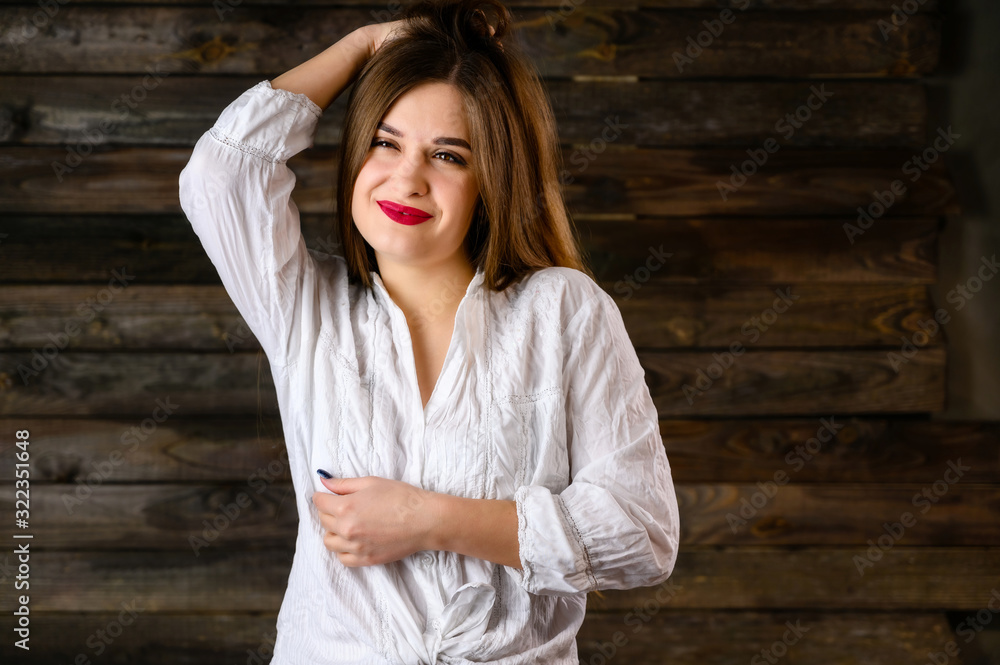 nice brunette girl with long hair with a smile in a white shirt rejoices on a wooden background, smiles and shows positive emotions