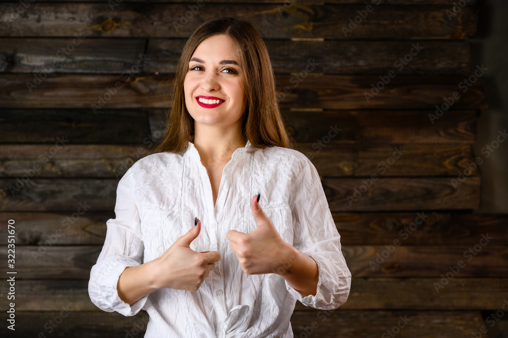 nice brunette girl with long hair with a smile in a white shirt rejoices on a wooden background, smiles and shows positive emotions nice brunette girl with long hair with a smile in a white shirt rejoices on a wooden background, smiles and shows positive emotions
