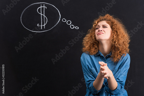 stressed redhead girl with dollar sign in thought bubble on chalkboard