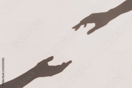 Grey shadows of hands reaching each other on the wall. Abstract blurred effect.