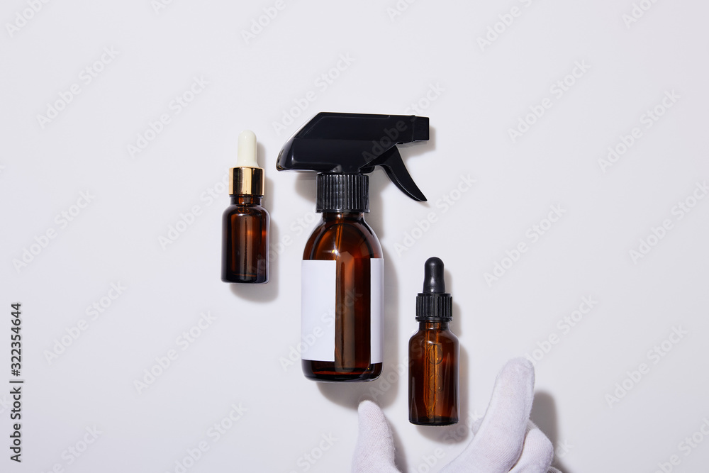 Cropped view of hand in glove with dispenser cosmetic bottles of oil on grey background Cropped view of hand in glove with dispenser cosmetic bottles of oil on grey background