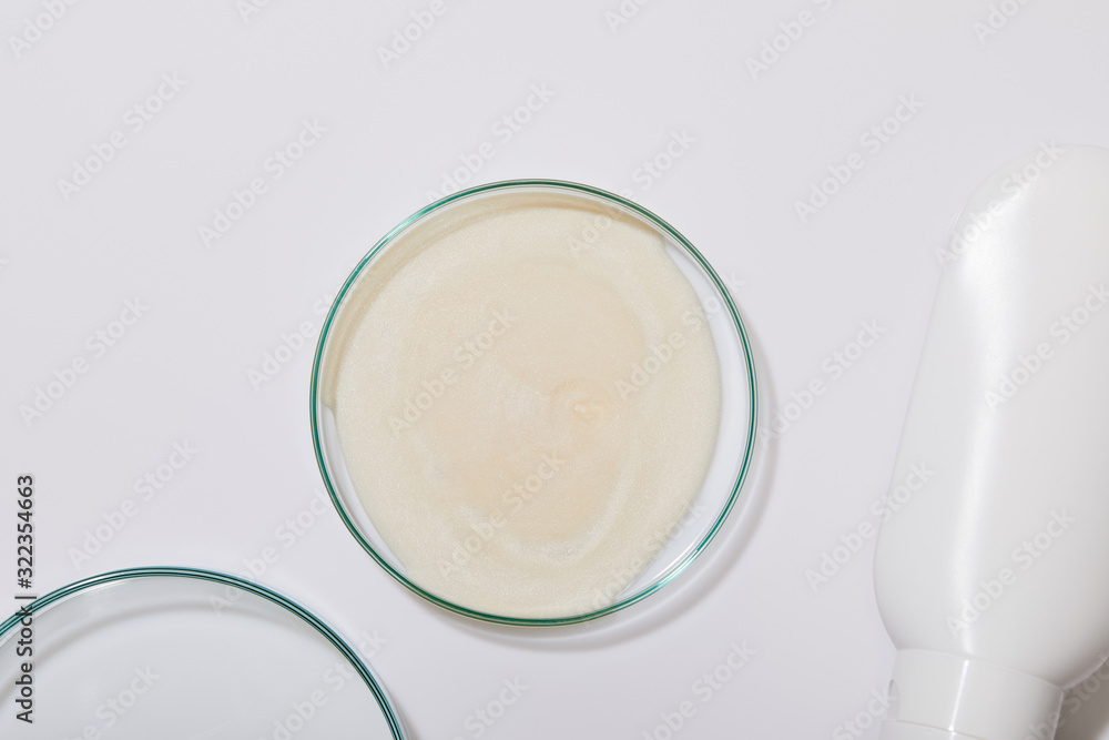 Top view of sample of cosmetic cream on laboraory glass next to tube on grey background Top view of sample of cosmetic cream on laboraory glass next to tube on grey background