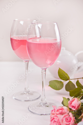 Two glasses with pink grape wine with rose flowers. Romantic dinner concept.