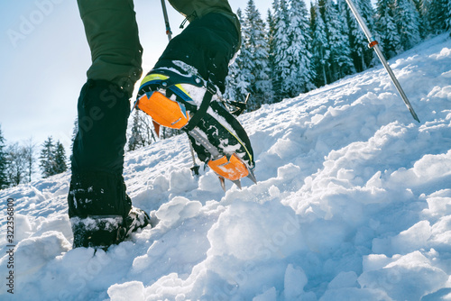 Bild auf Leinwand Close up shot of mountain boots with crampons and snow gaiters with snowy spruces on the background