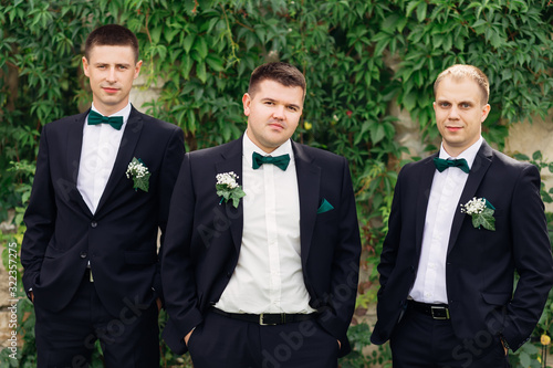 groom and groomsman in suits hold hands in pockets and looking a