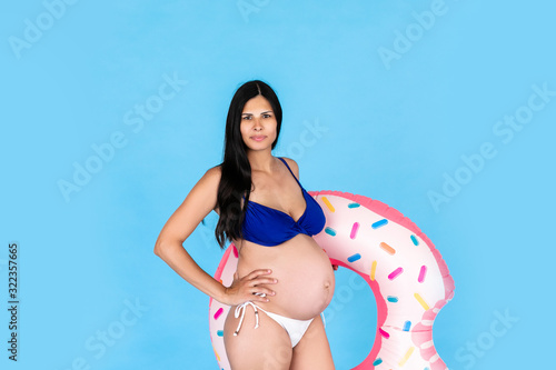 Happy pregnant women in swimsuit with swimming ring donut on a colored blue background