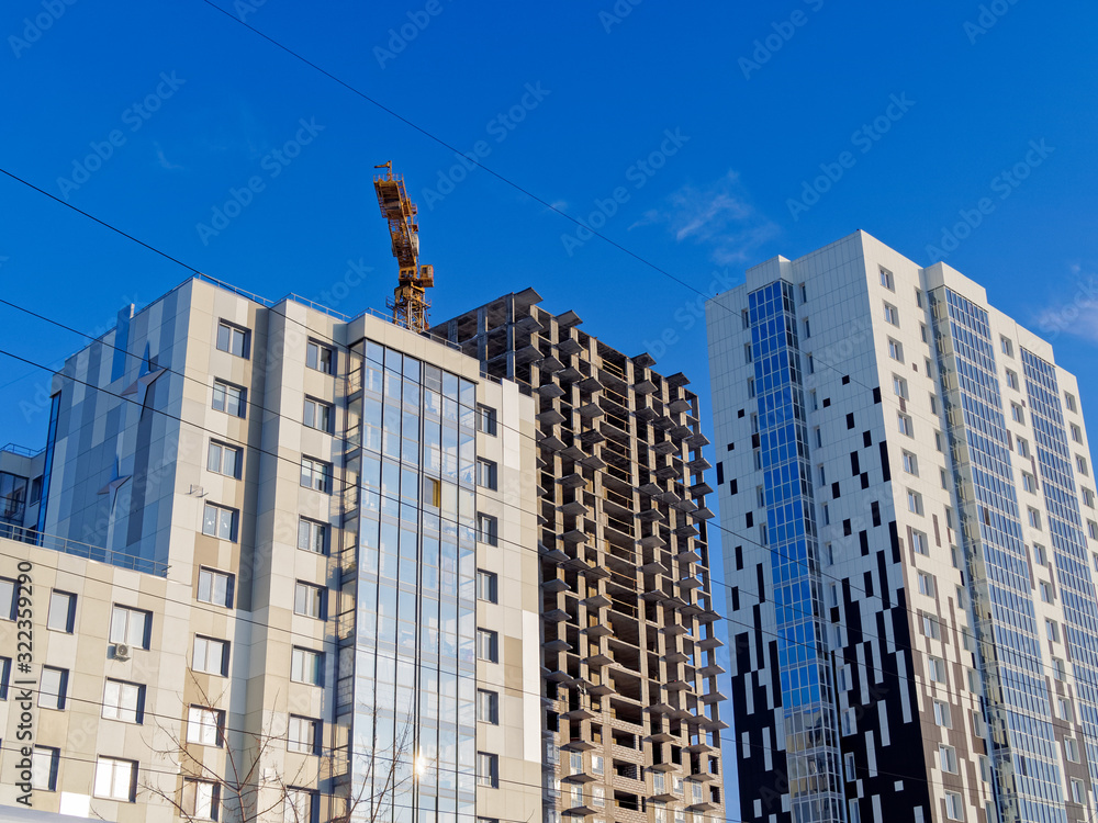 The construction of a multi-storey building. The design is made of reinforced concrete piles and floor slabs. A construction crane is under construction. Nearby are already built residential buildings