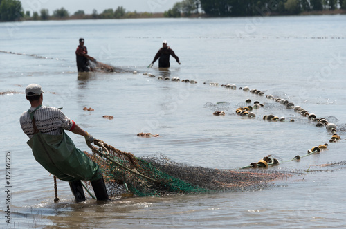 Obraz na plátně Fisherman drags and trawls the fishing net with fish in the river