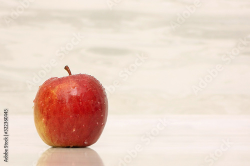 Red apple in drops of water on a beige wooden background.