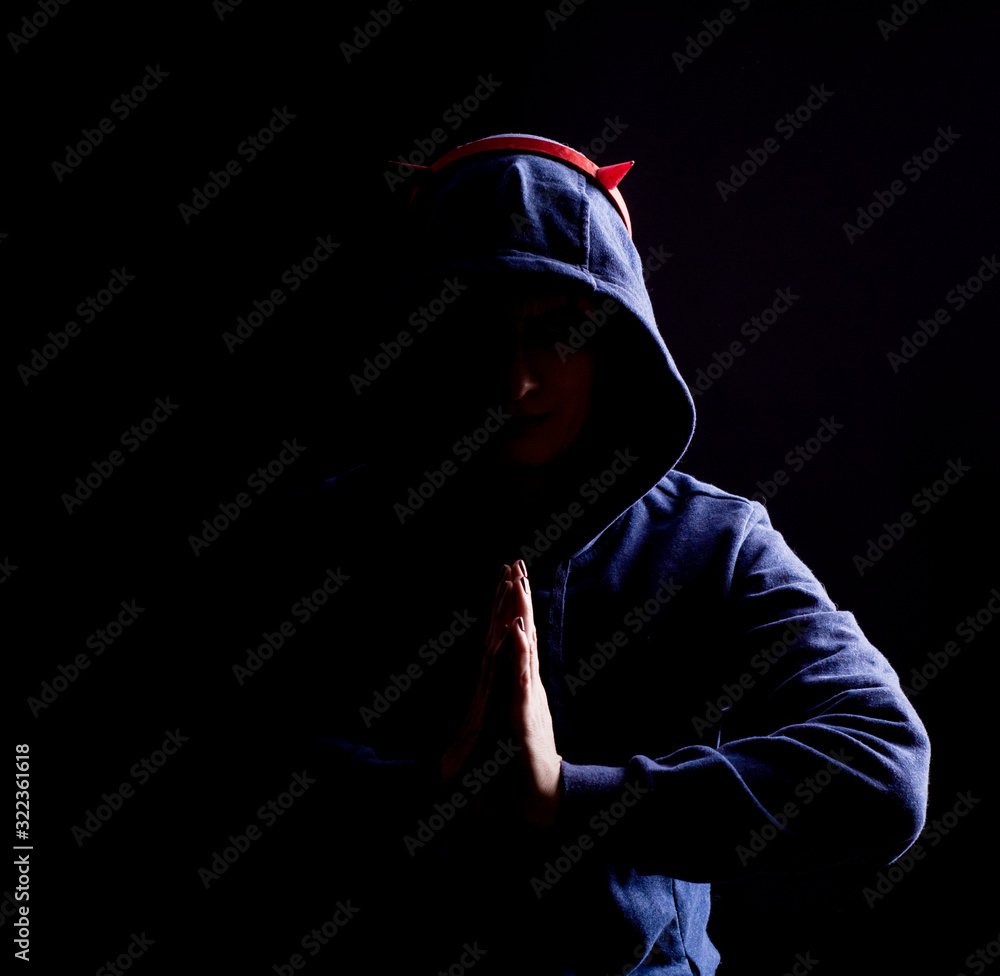 Shooting in the Studio. The girl in the hood holds her hands in front of her. Artificial horns on the head. Shooting in the Studio. The girl in the hood holds her hands in front of her. Artificial horns on the head.