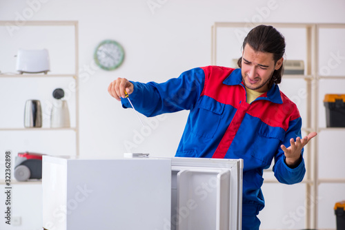 Young male contractor repairing refrigerator at workshop