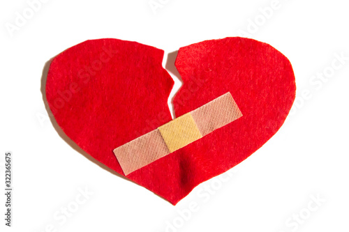 Broken heart and glued together with a band-aid. A heart from felt. A concept about broken love. Heart with plaster isolated on white background