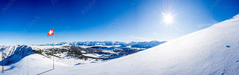 snow covered swiss alps mountain range with swiss national flag against blue sky, with copy space