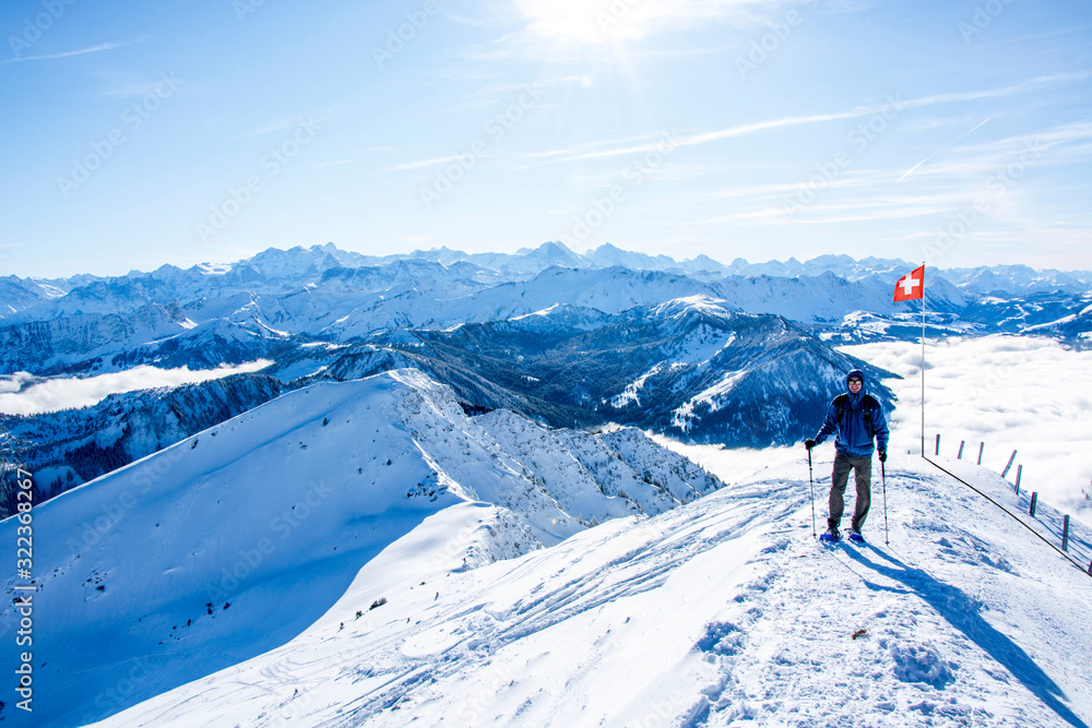 mountaineer against swiss alps mountain panorama in winter. hiker in front of snowy mountain panorama, blue sky swiss national flag