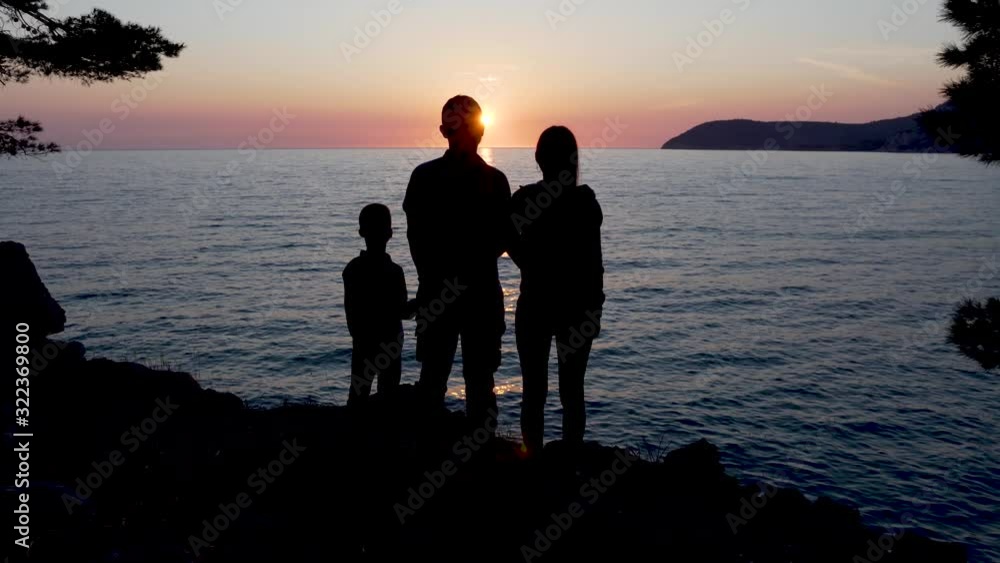 Silhouettes of a young family standing near the sea at sunset. Silhouettes of a young family standing near the sea at sunset.