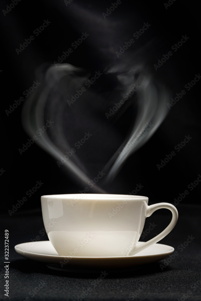 White cup of coffee on a black background. Steam in the shape of a heart over a cup of tea. White cup of coffee on a black background. Steam in the shape of a heart over a cup of tea.